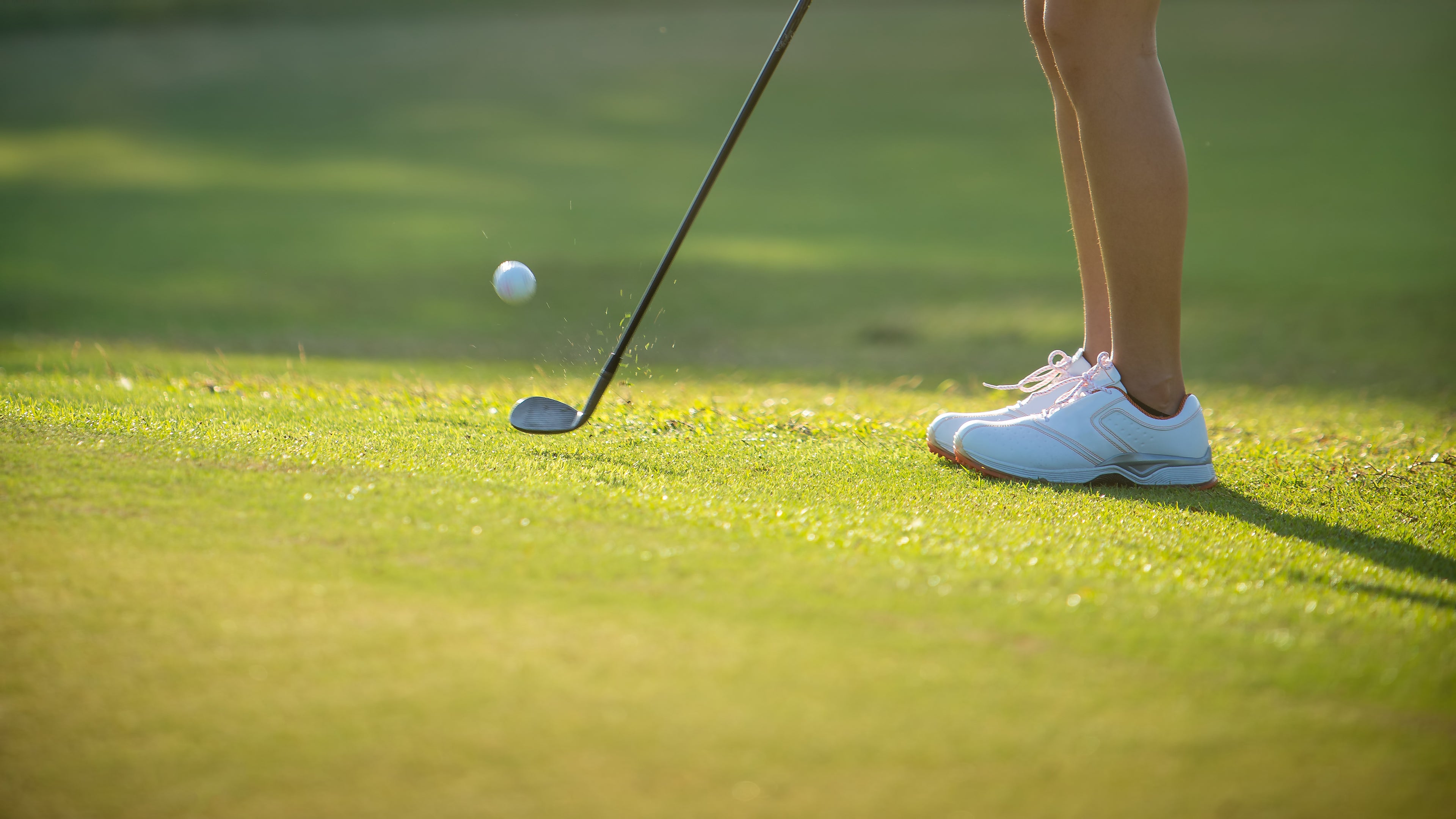 Girl chipping a golf ball onto a green on a golf course