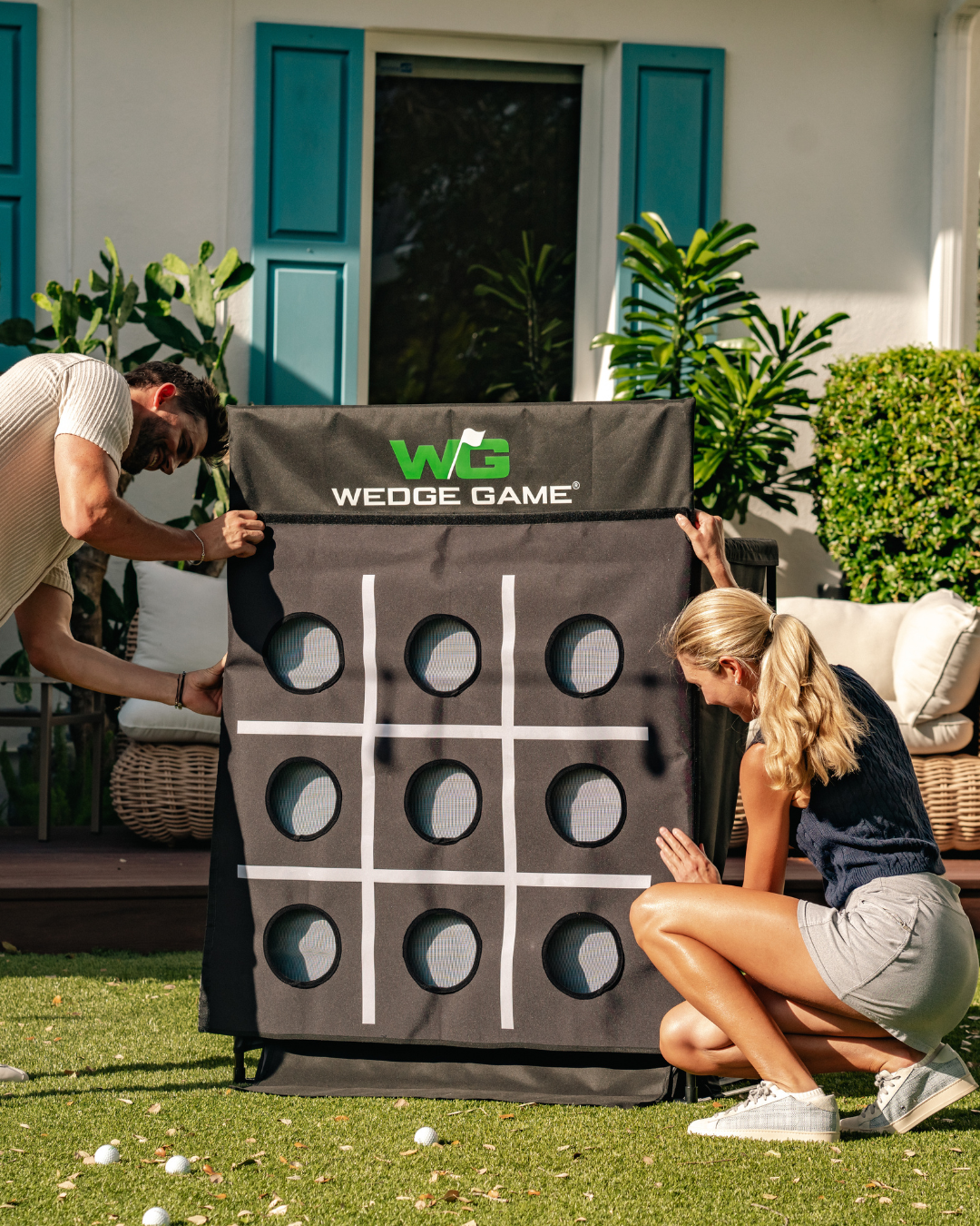 Two people setting up the WEDGE GAME short game net for practice in a backyard setting.